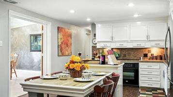 A modern kitchen with white cabinets, a dining area with a wooden table, and a view to a patio.