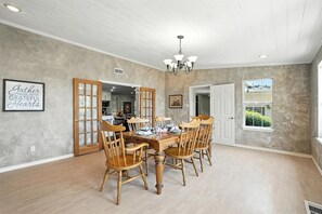 Une salle à manger avec une table et des chaises en bois, un lustre et une citation inspirante encadrée au mur.
