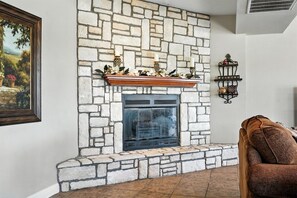 Une cheminée en pierre avec une étagère décorative, un tableau représentant un paysage encadré et un mur en pierre.