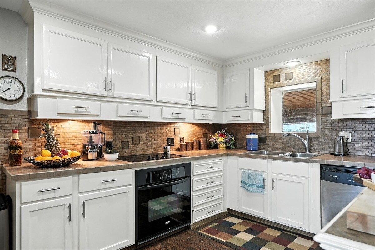 Una cocina con armarios blancos, horno negro, pileta y salpicadero de azulejos.
