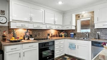 Una cocina con armarios blancos, horno negro, pileta y salpicadero de azulejos.