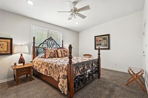 Ein Schlafzimmer mit einem Himmelbett, einem Nachttisch, einer Lampe, einem Stuhl, einem Deckenventilator und einem Fenster mit Jalousien.