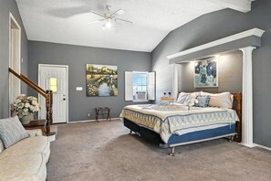 Een slaapkamer met een bed, een stoel, een trap en kunstwerken aan de wanden.