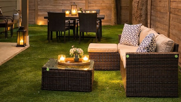Un patio al aire libre con mobiliario de mimbre, luces colgantes y velas.