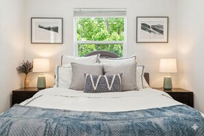 Ein ordentlich bezogenes Bett mit blauer Decke, zwei Nachttischlampen und gerahmten Bildern an der Wand.
