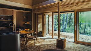 A modern kitchen with a central island, wooden flooring, and large sliding glass doors leading to an outdoor deck. - SANU 2nd Home Yatsugatake 3rd (Hokuto)