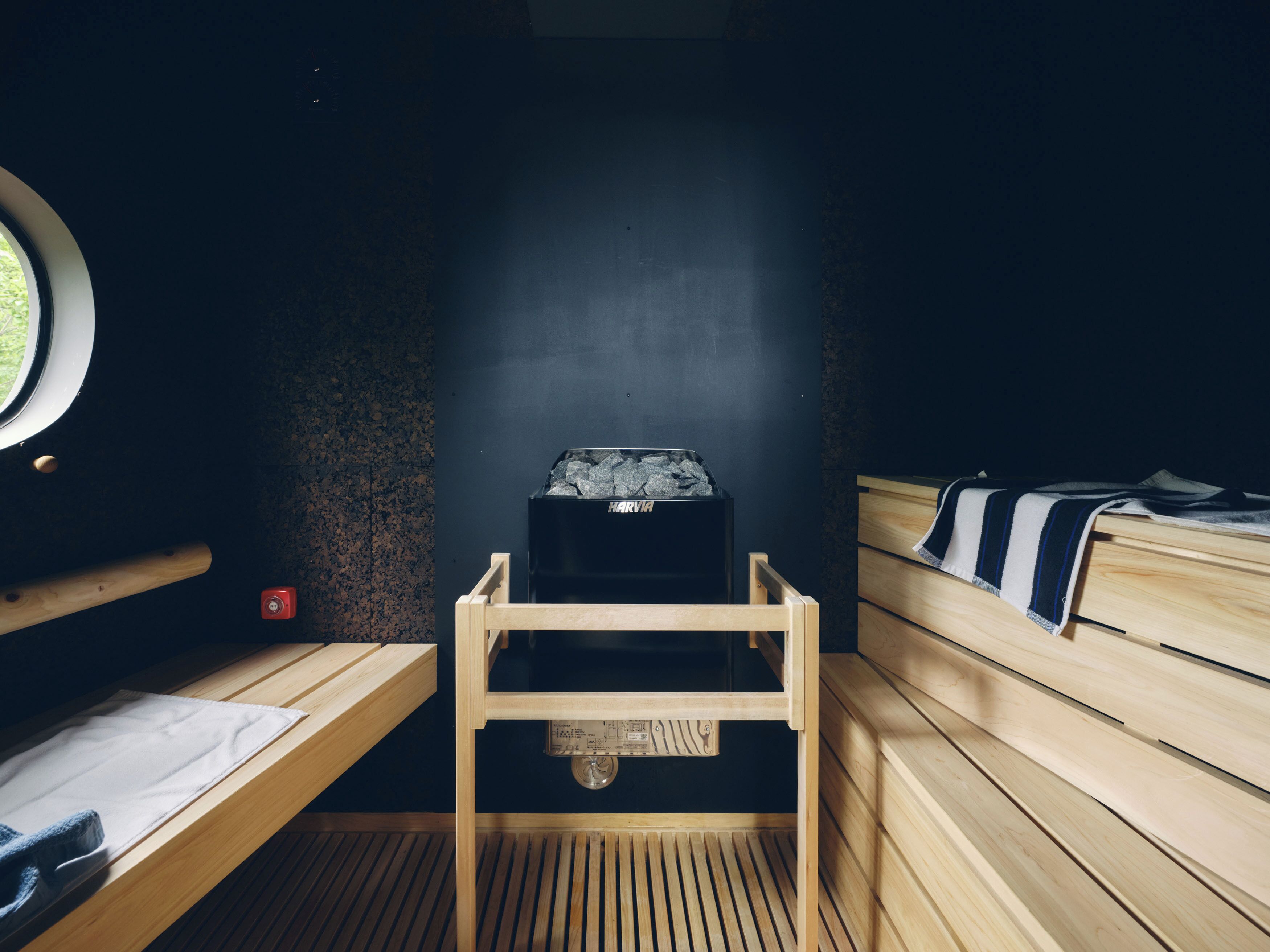 A sauna room with wooden benches, a sauna heater, and a window.