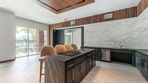 A modern kitchen with a central island, built-in appliances, and a large window overlooking a balcony. - Regards At Med Center 130 I Spacious 1 Bed 1 Bath (Houston)