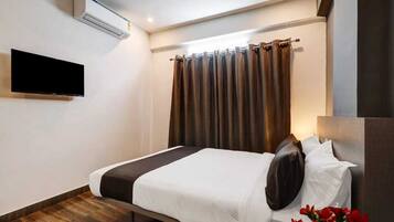 Habitación de hotel con cama, televisor de pantalla plana en la pared, ventana con cortinas y una mesita con un florero.
