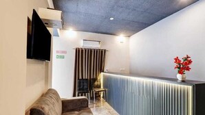 Ein modernes Hotelzimmer mit Sofa, einem kleinen Tisch, einer Rezeption und einem an der Wand montierten Fernseher.