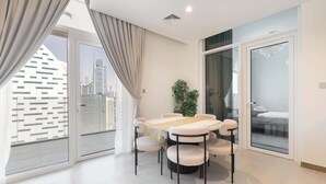 Uma sala de estar moderna com uma mesa redonda e seis cadeiras, janelas amplas com cortinas, um vaso de planta e vista para um horizonte urbano.