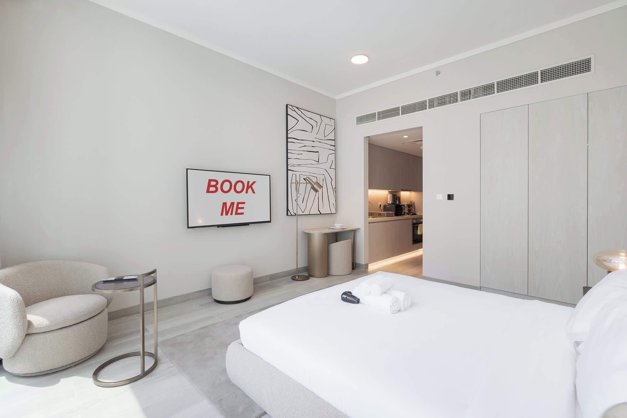 Une chambre d’hôtel moderne dotée d’un grand lit, d’un coin salon avec un fauteuil, une petite table et une œuvre d’art accrochée au mur.