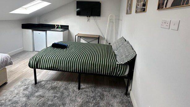 A bedroom with a bed, a TV mounted on the wall, and a skylight. - Bright Studio in Thornton Heat (Thornton Heath)