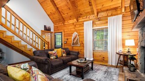 A cozy log cabin interior with a wooden staircase, a brown leather sofa, a coffee table, and a fireplace. - Timber & Tranquility Cabin (Pine Mountain)