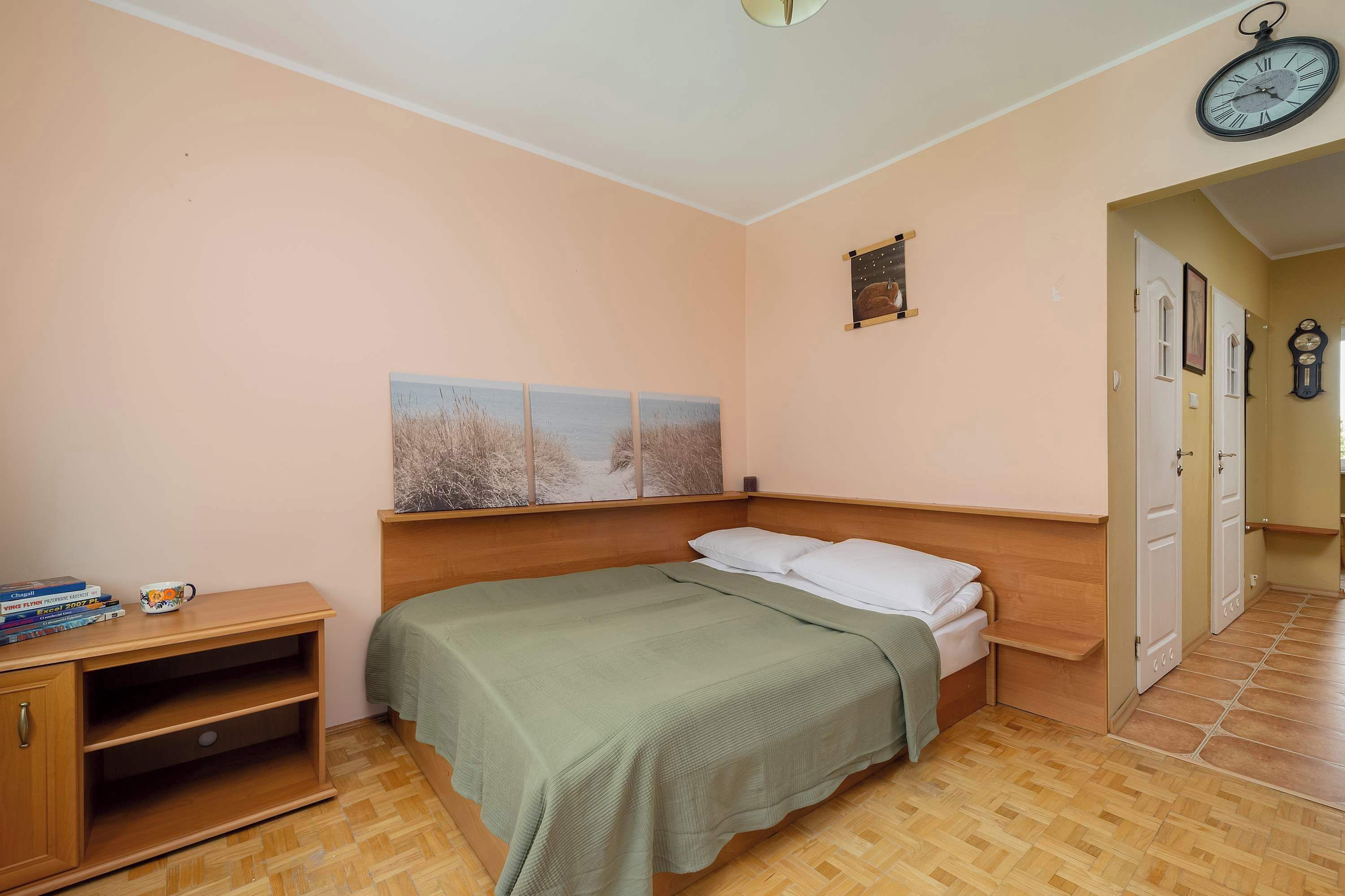 A bedroom with a bed, a nightstand, a wall clock, and a door.