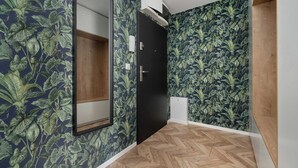 A hallway with a mirror, a door, and a wall with a leafy pattern.