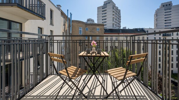 A balcony with a table and chairs, overlooking a cityscape with buildings.