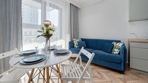 A modern living room with a dining table set for two, a blue sofa, and a small cabinet.