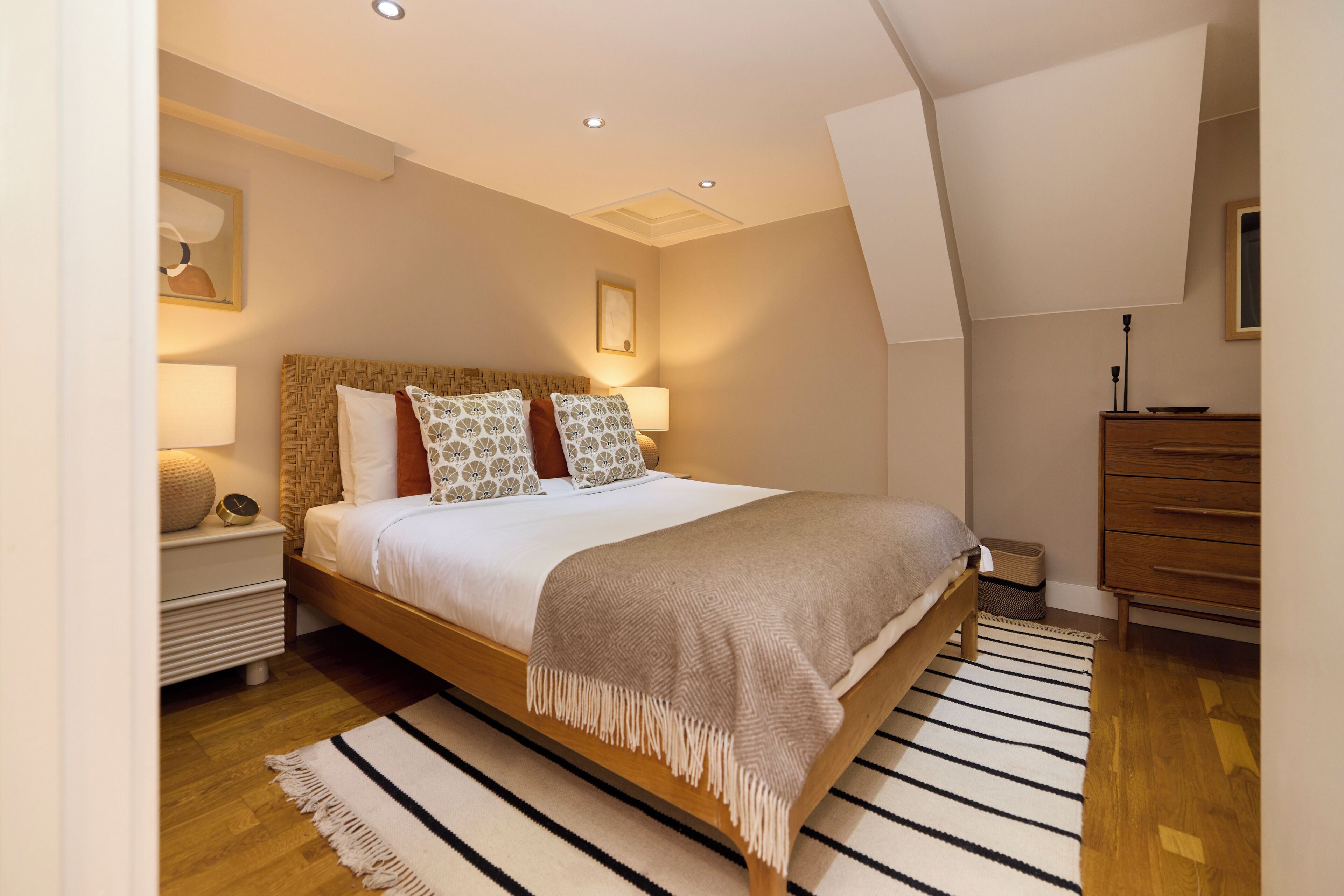 Un dormitorio moderno con una cama de madera, una mesita de noche blanca, un aparador de madera y un tapete a rayas.