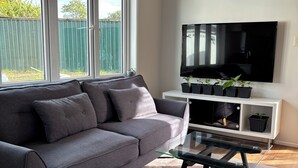 Een moderne woonkamer met een grijze bank, een glazen salontafel en een flatscreen televisie aan de wand bevestigd.