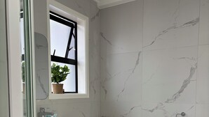 Een badkamer met een marmeren wand, een houten wastafelmeubel, een toilet en een raam met een bloempot.