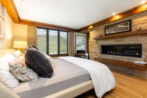 A bedroom with a bed, a fireplace, a large window, and a stone wall.