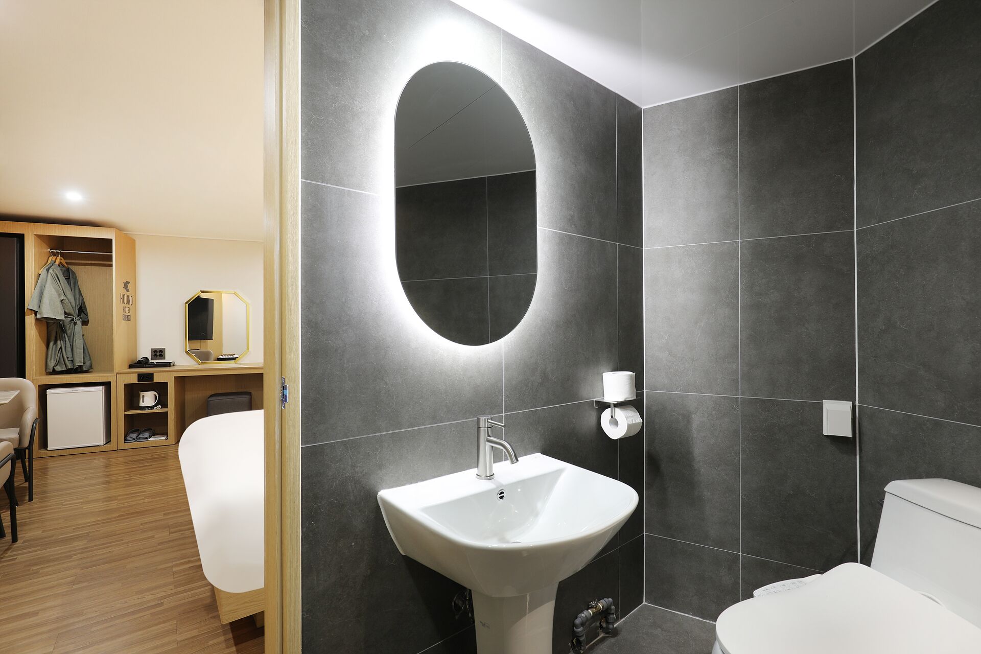 A modern bathroom with a large oval mirror, a white sink, and a toilet.