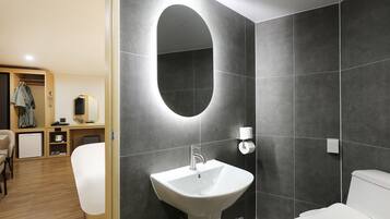 A modern bathroom with a large oval mirror, a white sink, and a toilet.