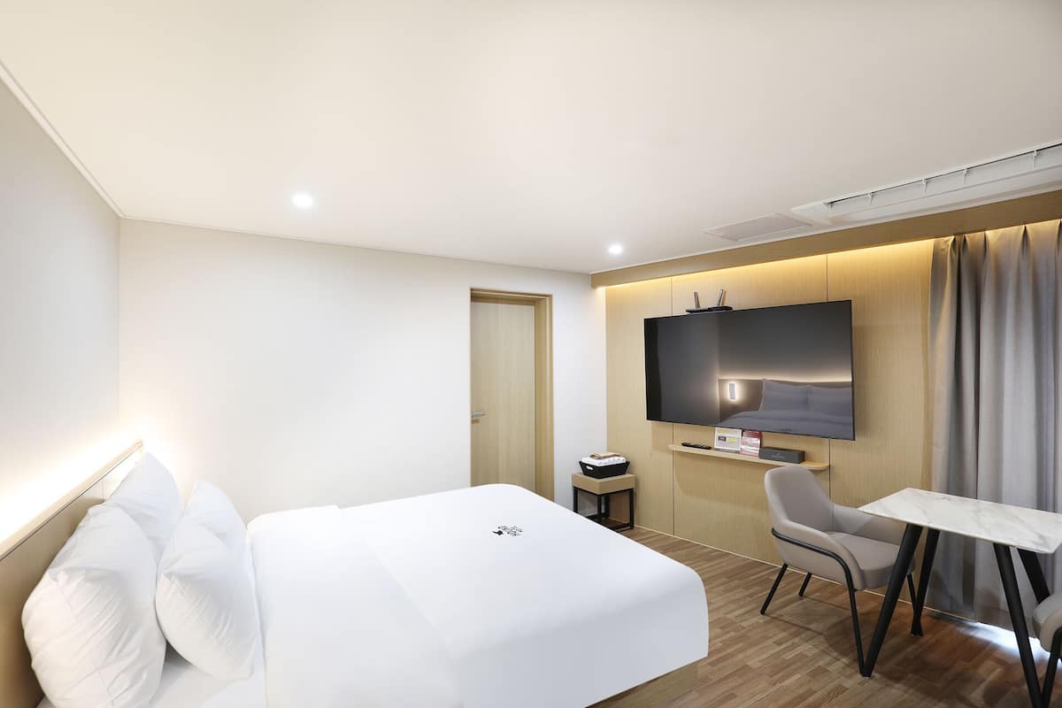 Una habitación de hotel con cama, escritorio, silla, televisor y puerta.
