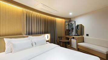 A hotel room with a bed, a seating area, a mirror, and a wall-mounted air conditioning unit.