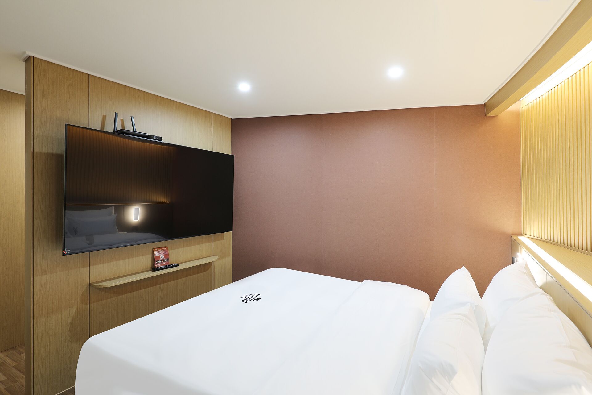 Una habitación de hotel con una cama, un televisor instalado en un mueble de madera y una pared marrón.