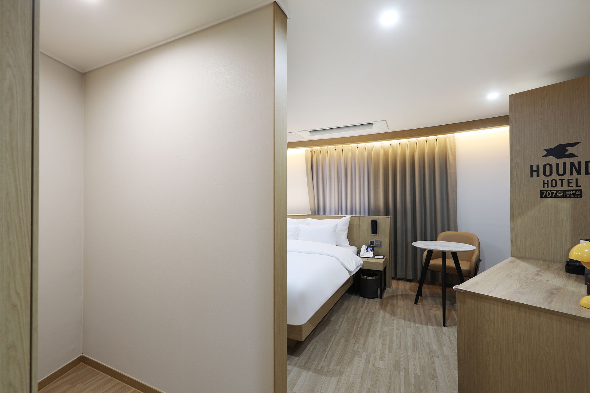 A hotel room with a bed, bedside table, chair, and a desk with a telephone.