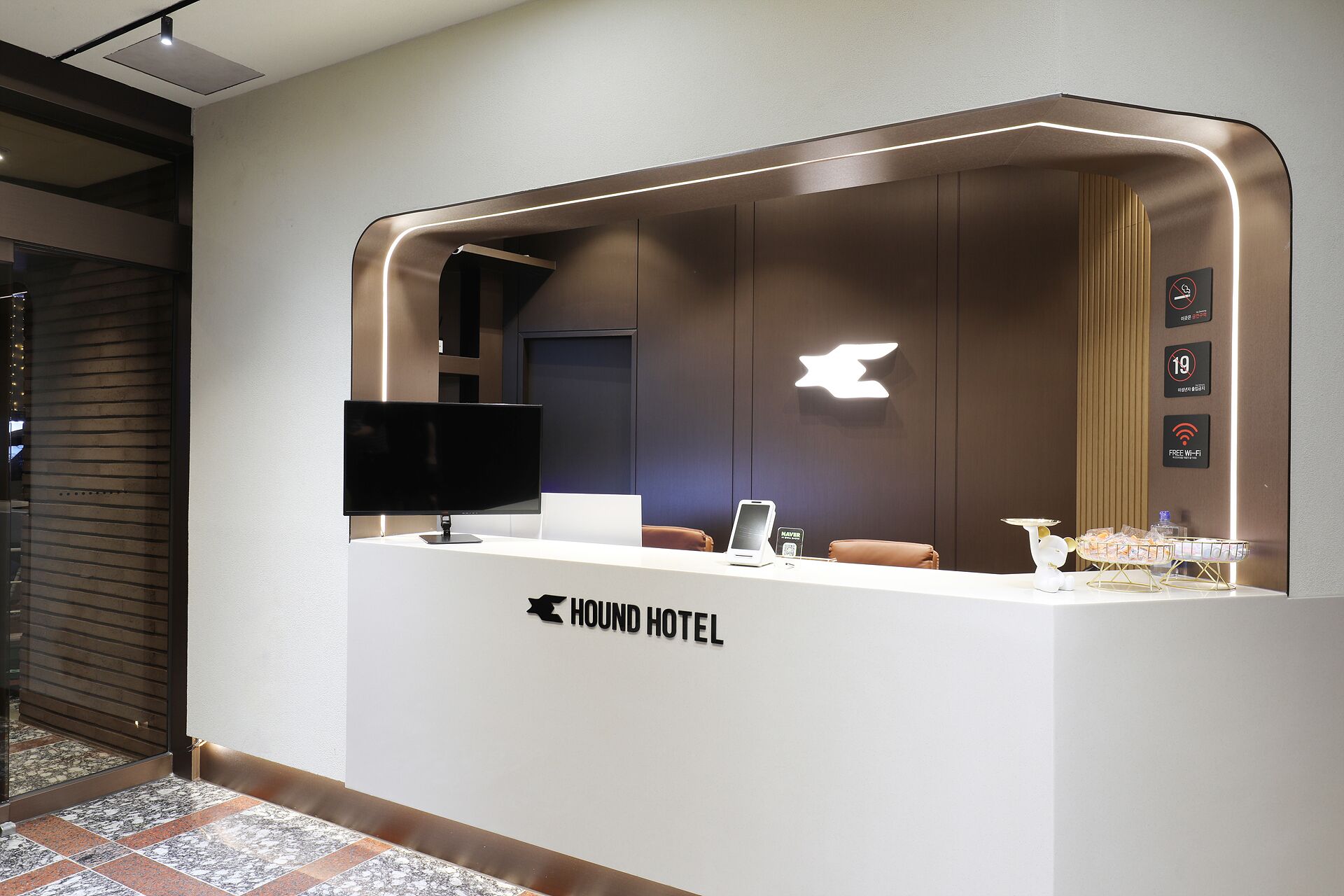 Un comptoir d’accueil au design moderne, un téléviseur à écran plat et un panneau indiquant que le Wi-Fi est gratuit.