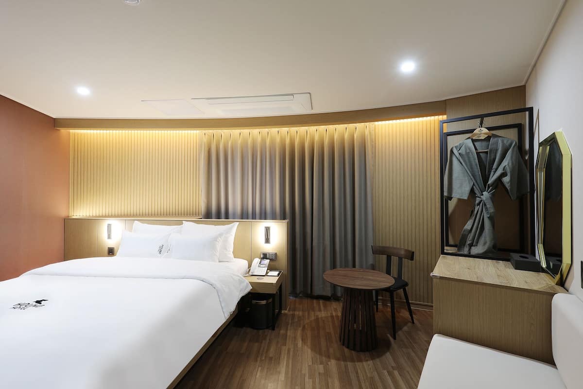 Habitación de hotel con una cama grande, mesitas de noche, un escritorio, una silla, una mesa redonda, un espejo y una bata colgada en un perchero.