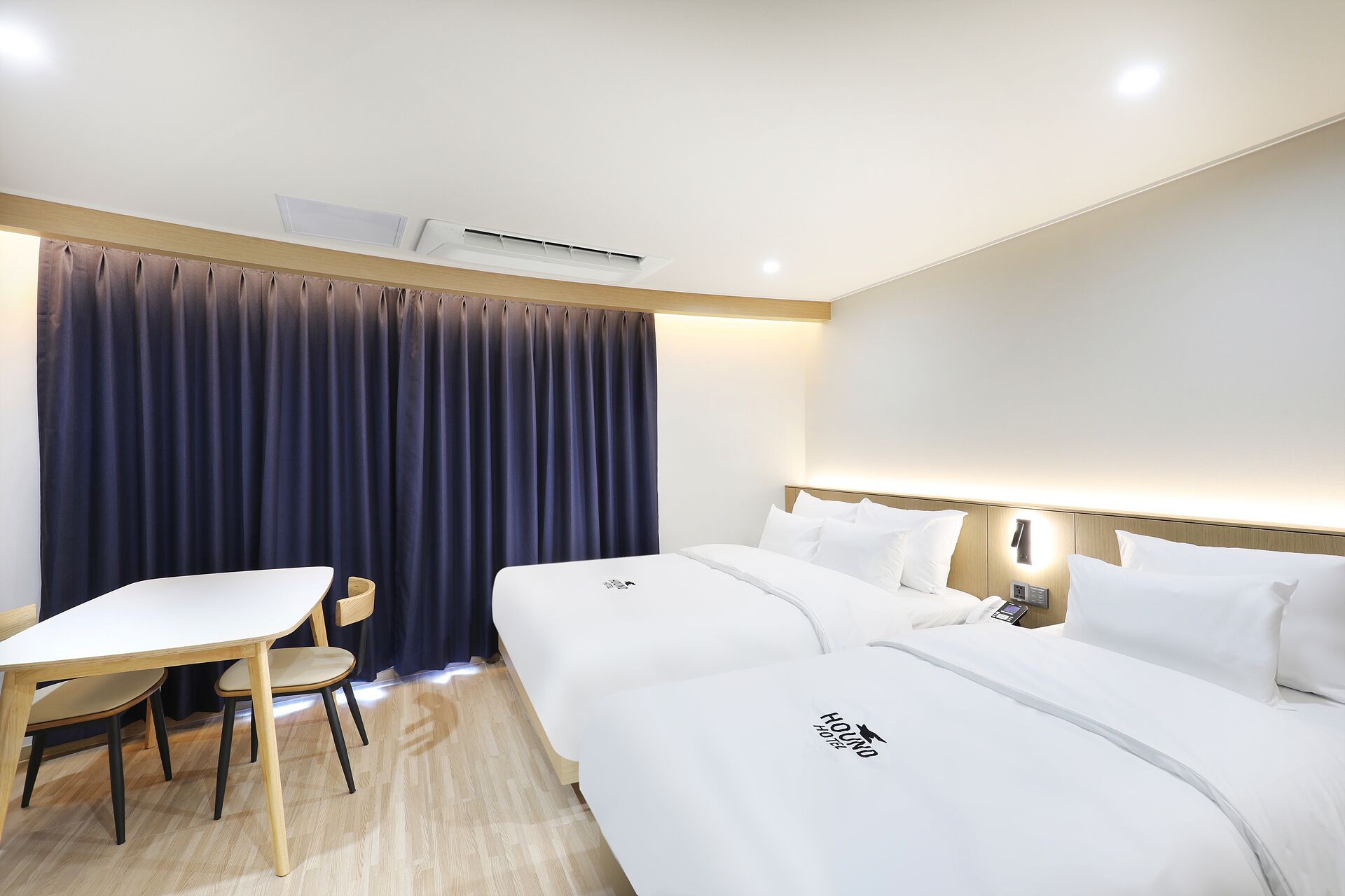 A hotel room with two beds, a desk, a chair, and a large window with curtains.