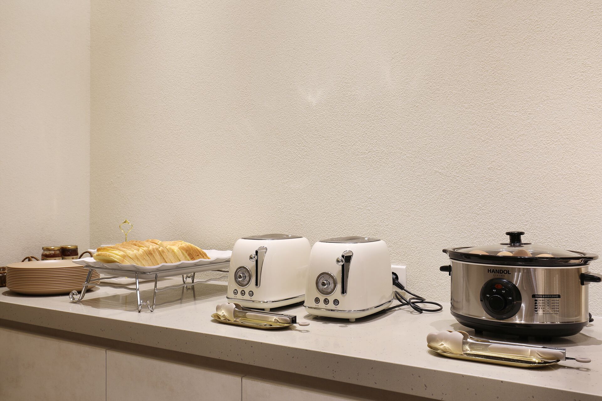 A kitchen counter with a bread basket, two toasters, and a slow cooker.