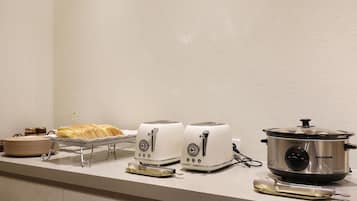A kitchen counter with a bread basket, two toasters, and a slow cooker.