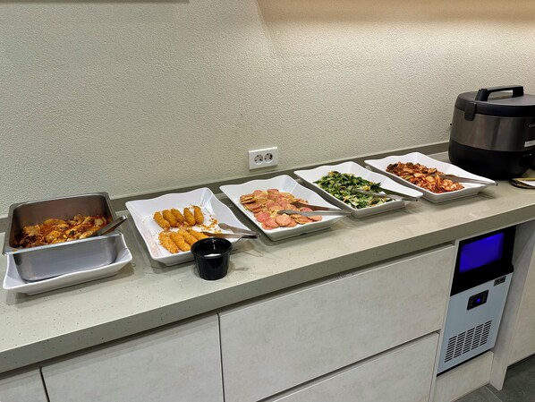 Una barra de buffet con distintos platos, una taza de café y una olla arrocera.