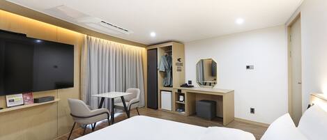 Habitación de hotel con cama, escritorio, silla, televisor, espejo y armario.