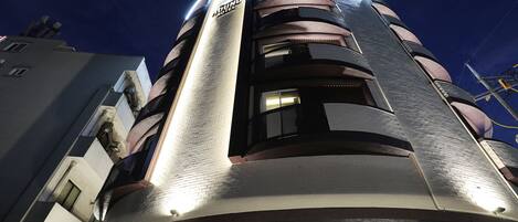 A modern hotel with a curved facade, multiple balconies, and a prominent entrance with a glass canopy.