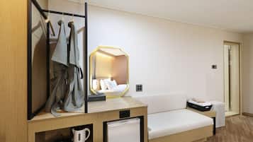 Habitación de hotel con cama, una mesita con hervidor y cafetera, espejo y perchero.