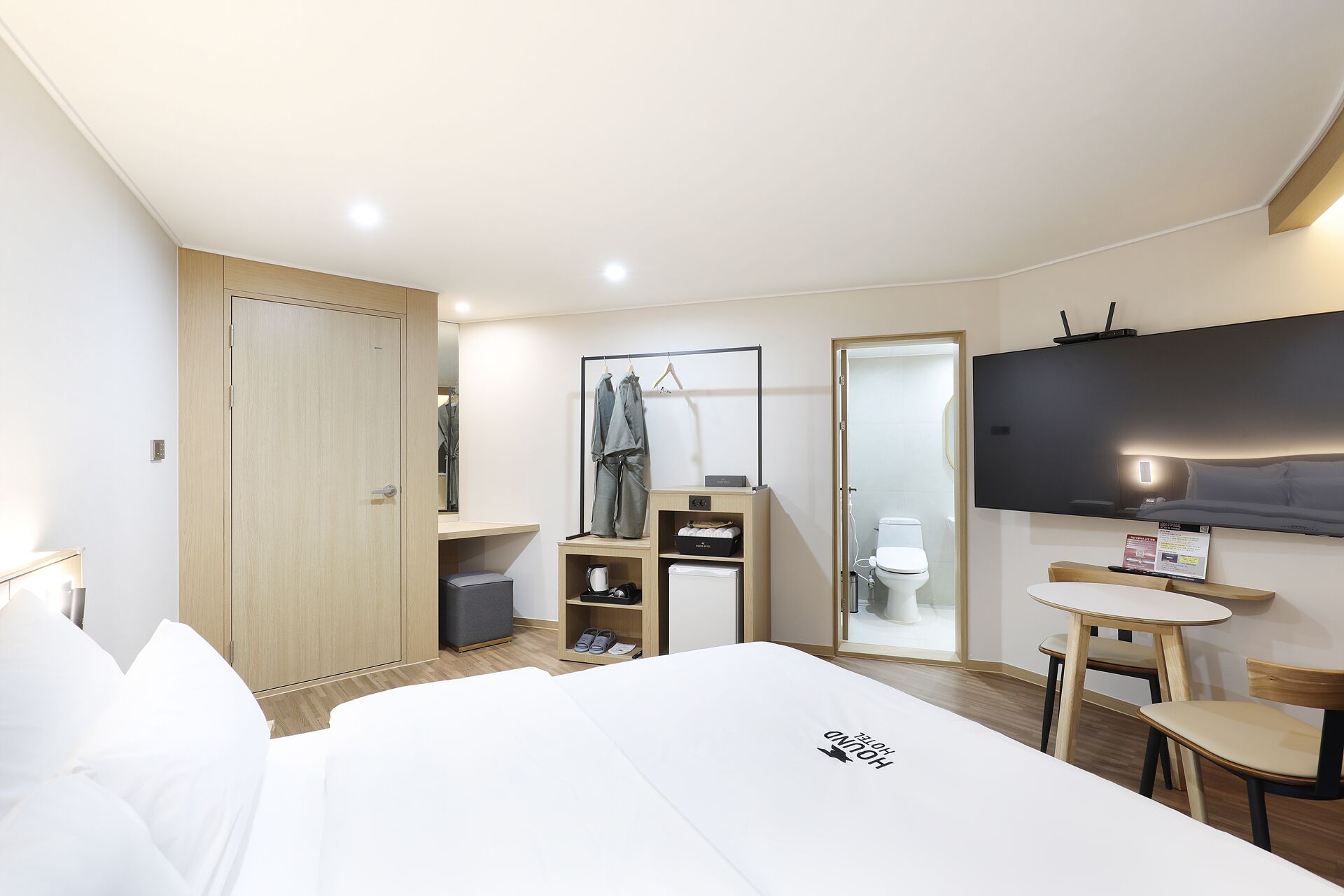 Quarto de hotel com cama, escrivaninha, cadeira, guarda-roupa, espelho e televisão.
