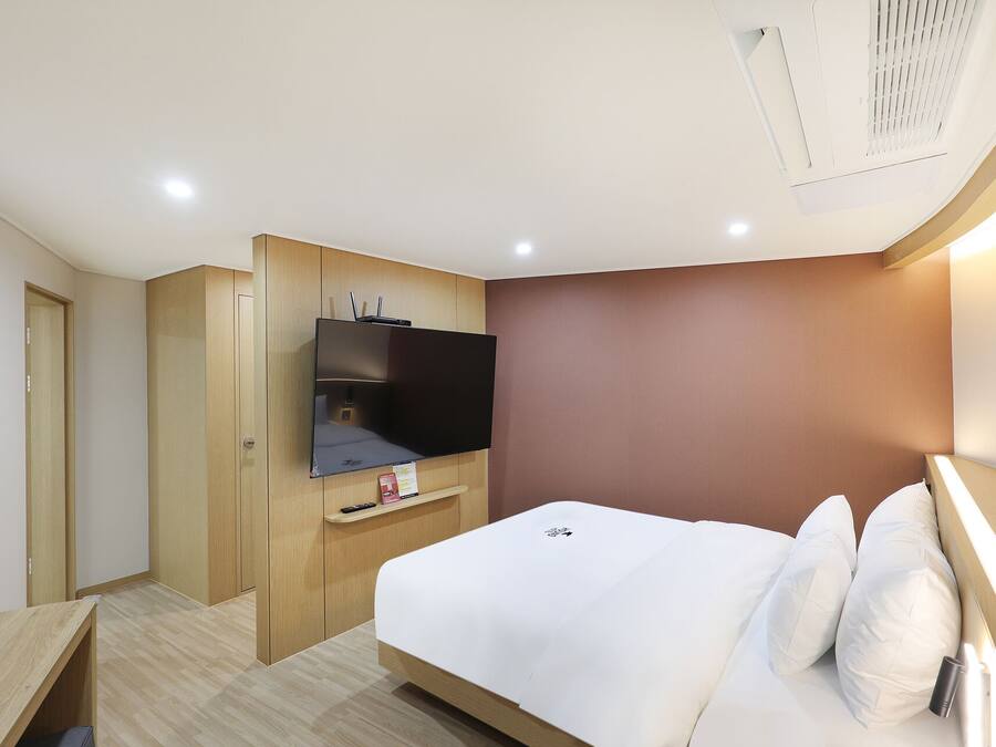 Una habitación de hotel con una cama, un televisor fijado en un mueble de madera, una mesita y una puerta.
