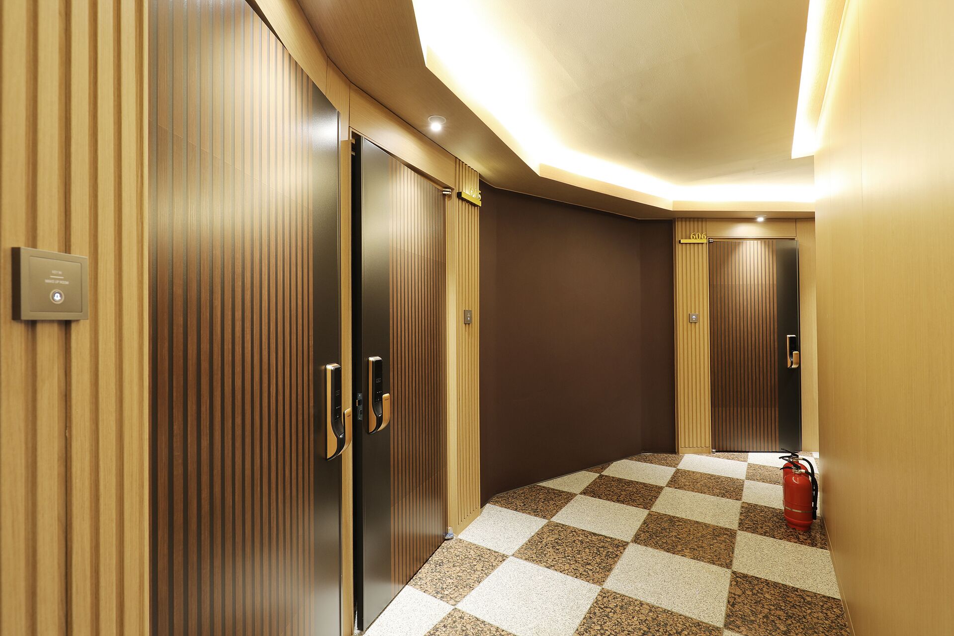 A hallway with checkered flooring, wooden panel walls, and a fire extinguisher.