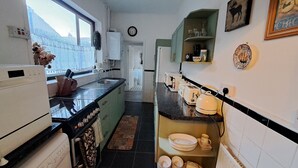 A narrow kitchen with a black countertop, white cabinets, and a small island with dishes.