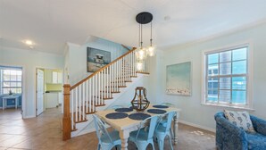 A dining area with a wooden staircase, a table with blue chairs, and a blue sofa. - Blue Haven Beach House: 3BR/3BA Pool Home Steps to Beach (Holmes Beach)