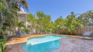 A swimming pool with a curved edge, surrounded by a brick patio and lounge chairs. - Blue Haven Beach House: 3BR/3BA Pool Home Steps to Beach (Holmes Beach)