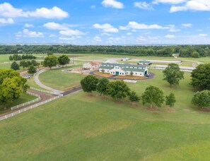 A large, open facility with multiple buildings, surrounded by expansive green fields and trees.