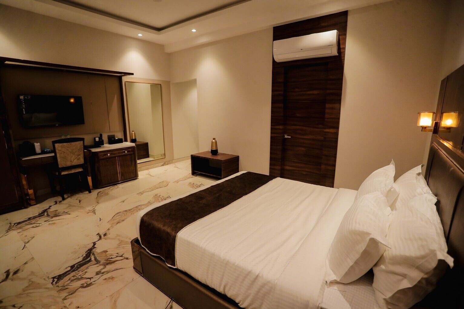 Una habitación de hotel con una cama grande, un escritorio con silla, un espejo y un televisor.