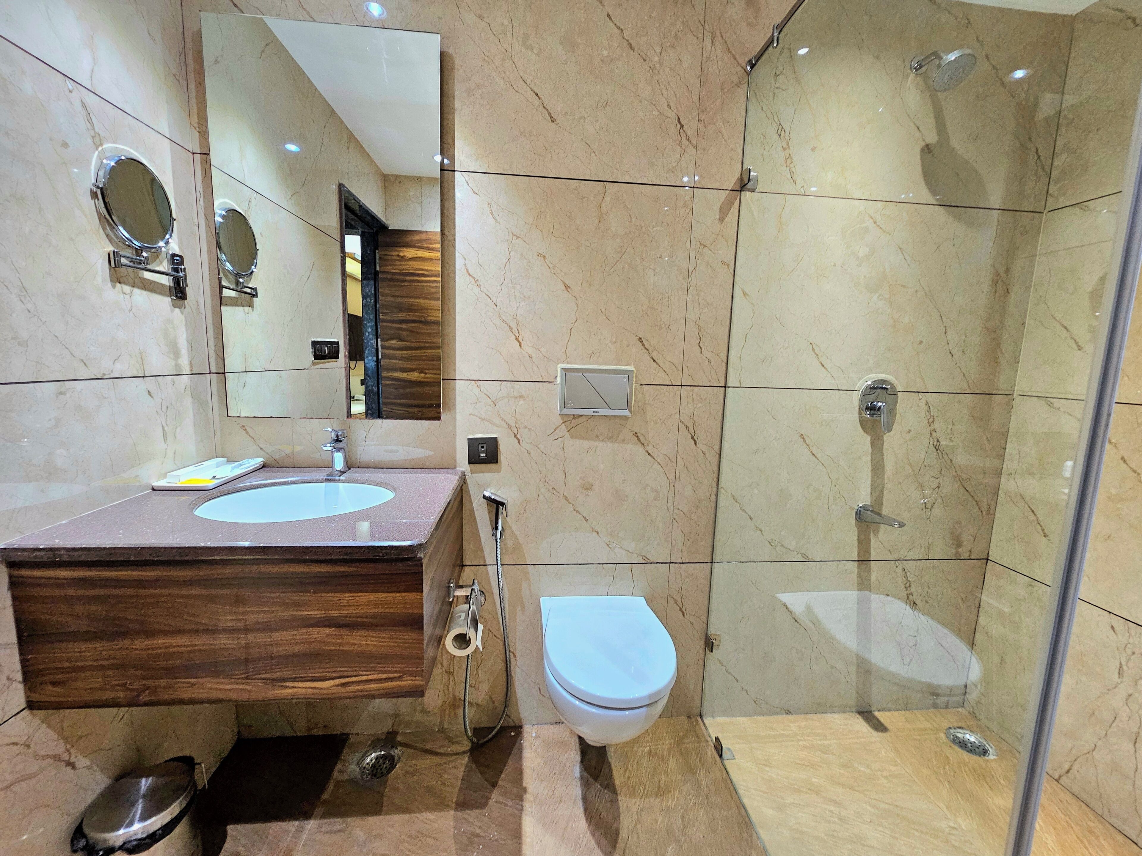 Un baño moderno con tocador de mármol, inodoro, ducha con mampara de vidrio y un espejo grande.